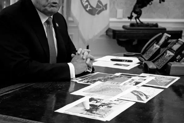 A black and white picture of half of Donald Trump's face with various documents scattered across the desk.